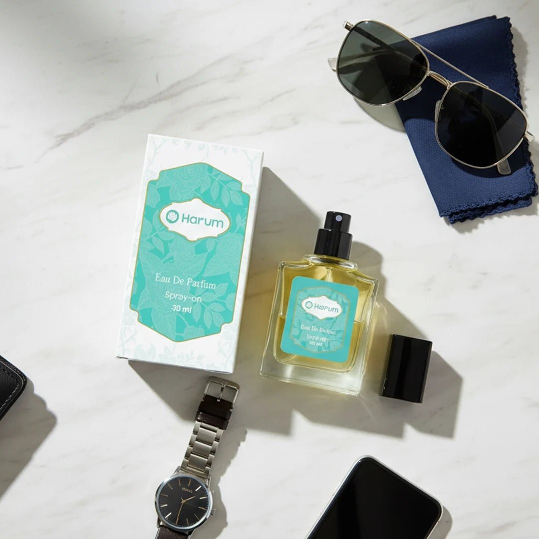 Harum Eau De Parfum 30ml perfume bottle and teal box flat lay with watch and sunglasses on marble surface