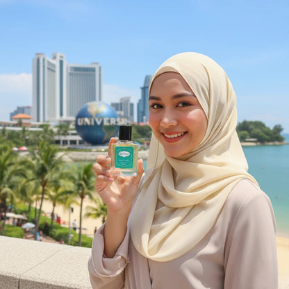 A smiling woman in a beige hijab holding a Harum.sg perfume bottle at Universal Studios Singapore with clear blue sky and palm trees in the background.