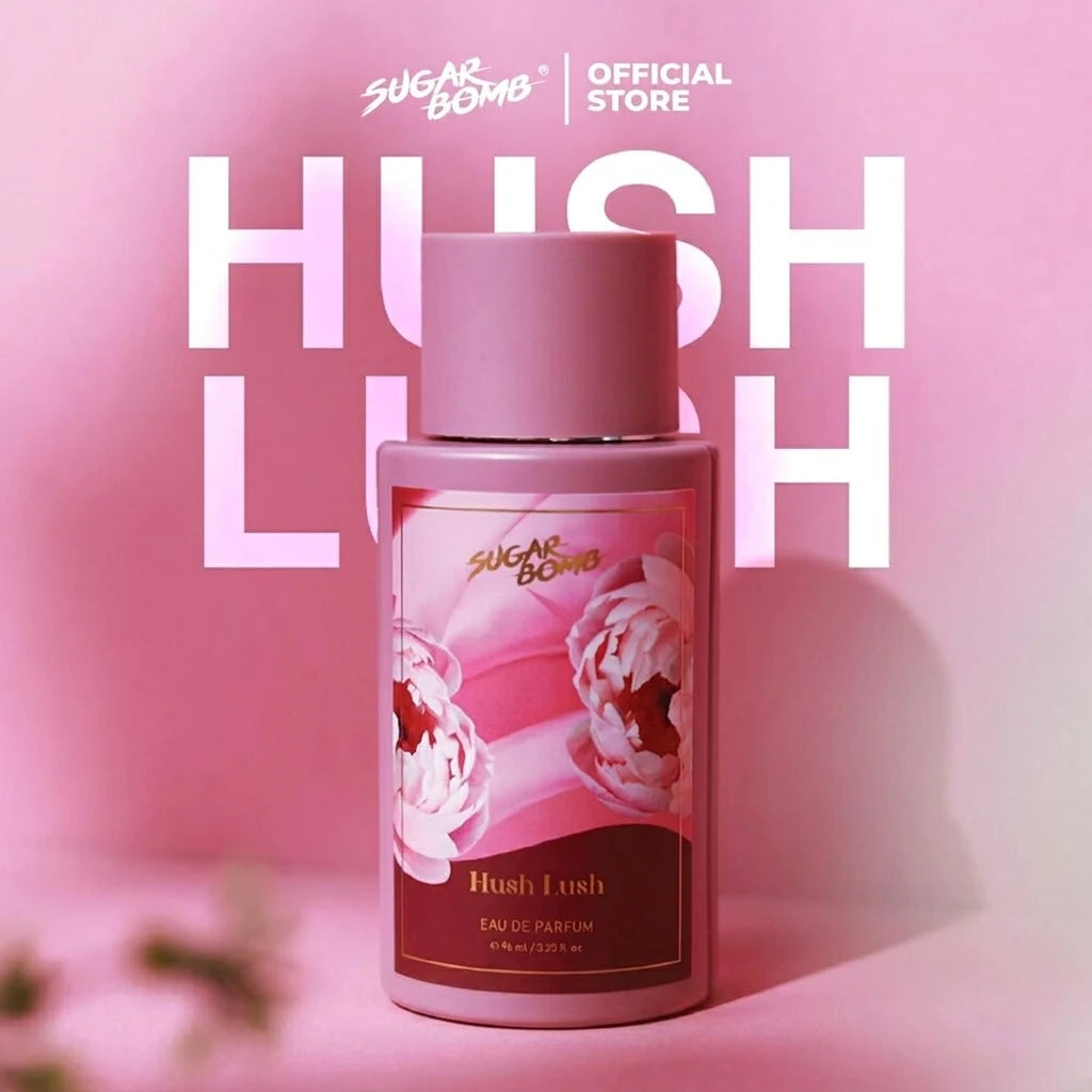 SugarBomb Hush Lush Eau de Parfum bottle in a matte pink casing, featuring a floral label with pink peonies, set against a pastel pink background with the words "HUSH LUSH" in large white typography.