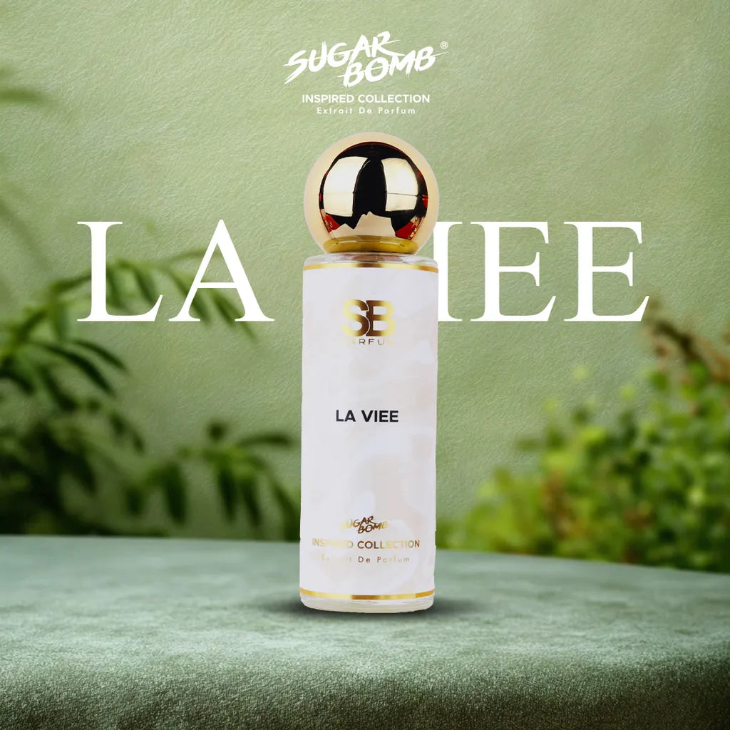 SugarBomb La Viee Extrait De Parfum from the Inspired Collection, a sweet gourmand fragrance inspired by Lancôme La Vie Est Belle, set on a soft green surface with a botanical background.